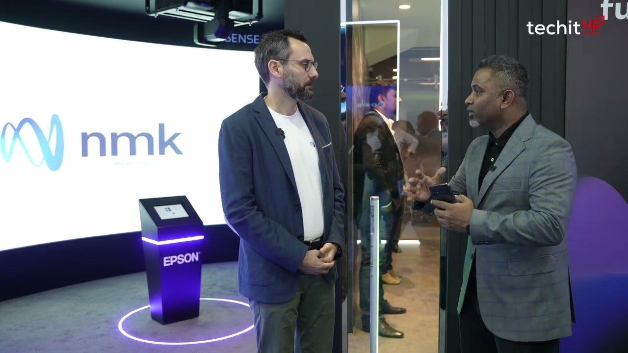 two men in suits talking to each other in front of a large screen