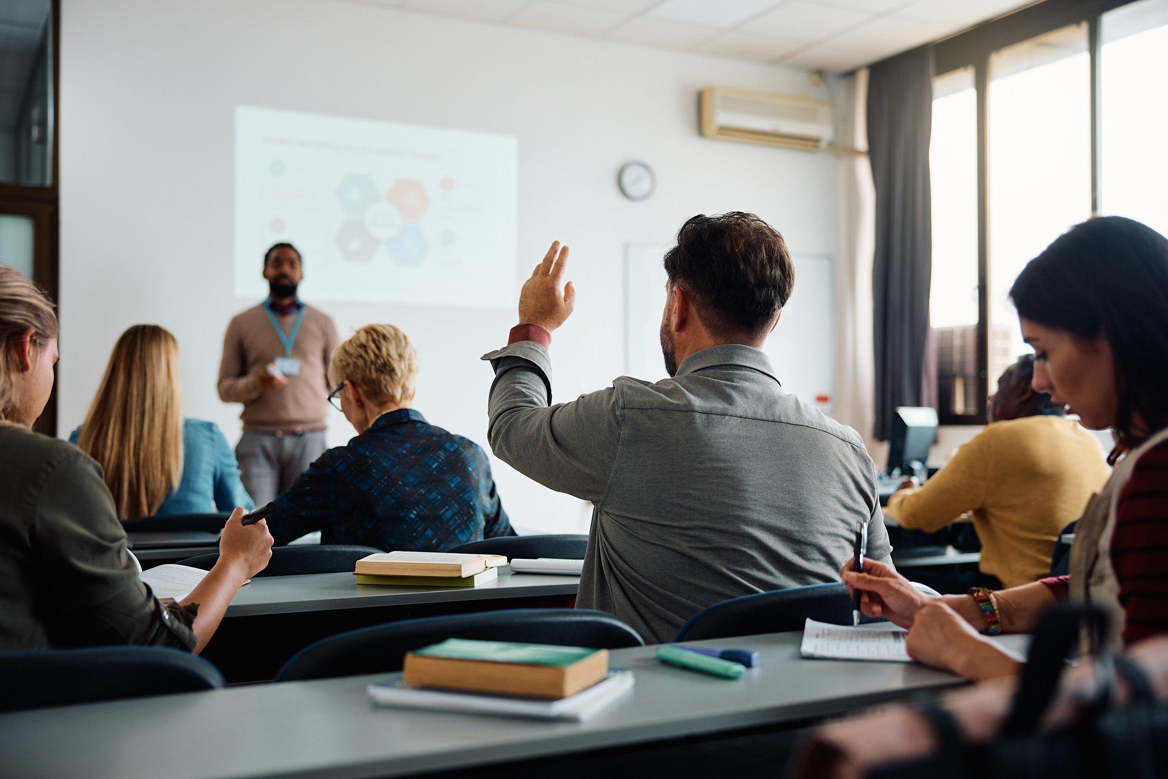 a group of people sitting in a classroom with one person raising his hand