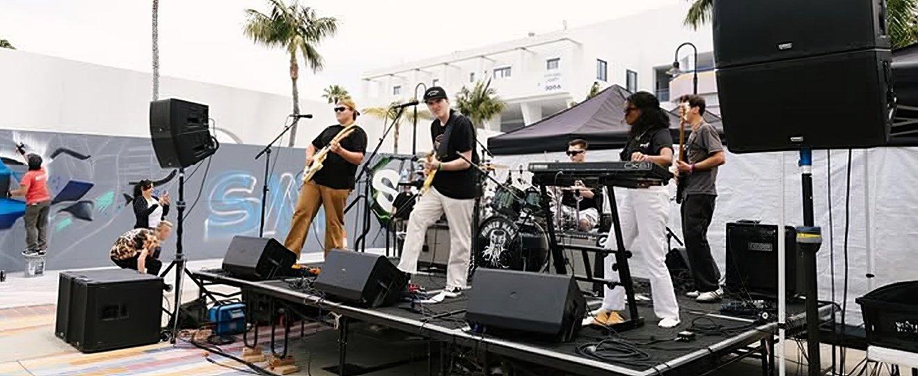 a group of people are playing music on a stage in a parking lot