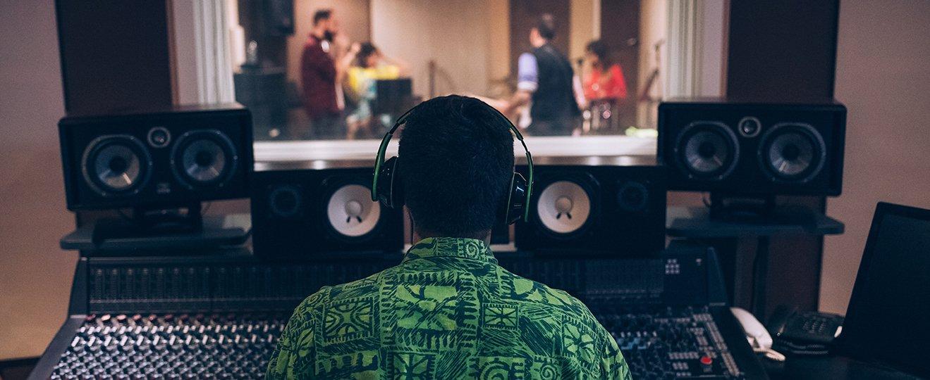 a man in a green shirt sitting at a mixing board
