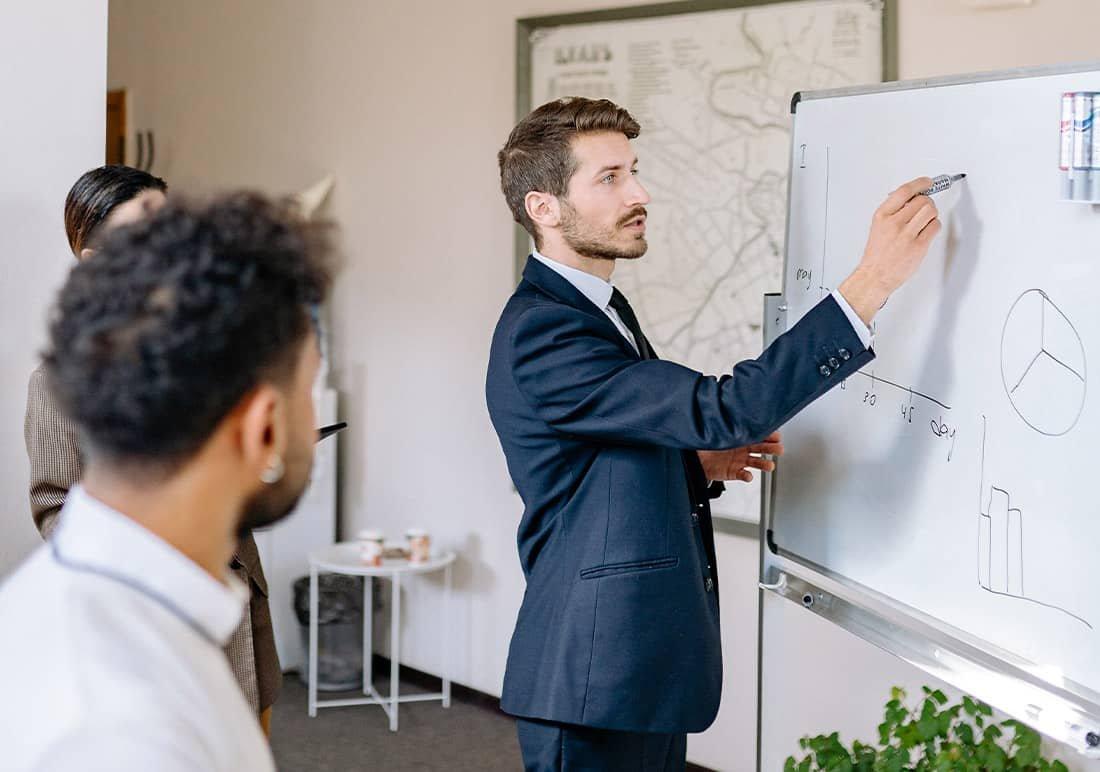 a man in a suit writing on a whiteboard in a business meeting