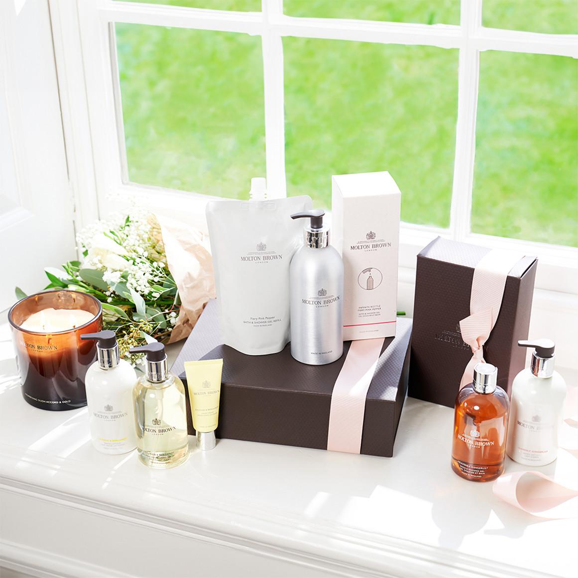 Molton Brown products displayed on a windowsill with candles, bottles, and ribboned packaging.