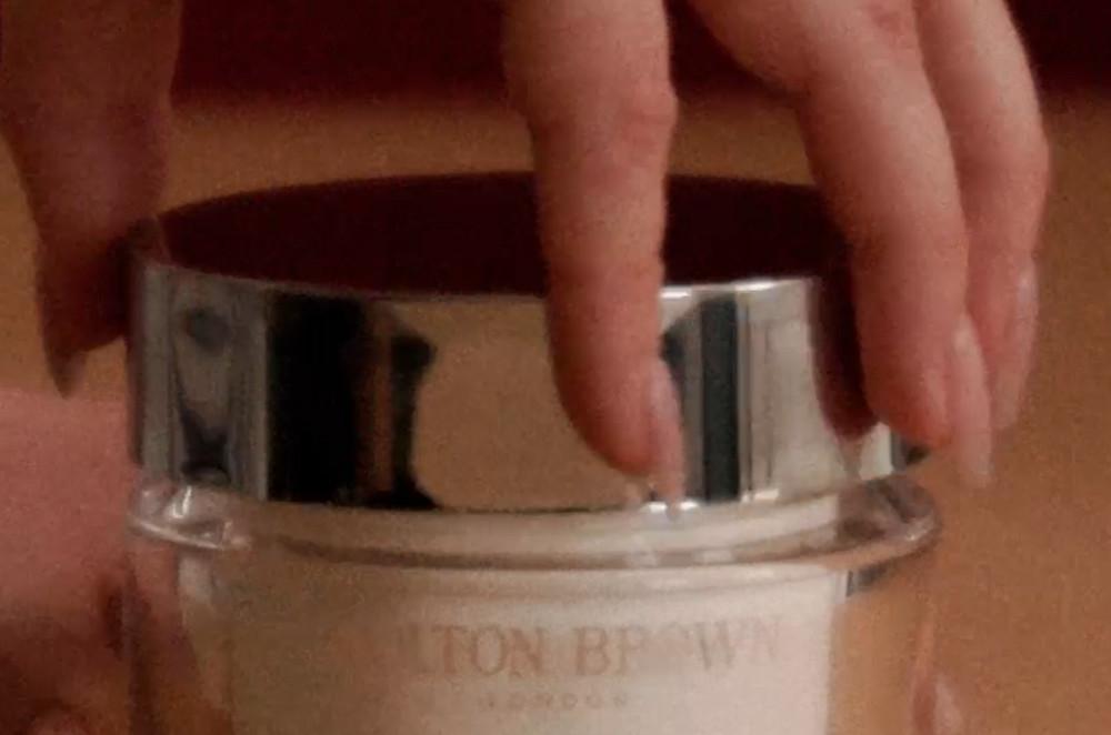 an image of a body cream glass bottle is being opened