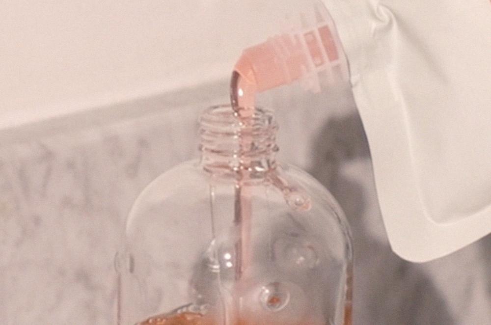 An image of hand wash refill pouch is refilling a hand wash glass bottle
