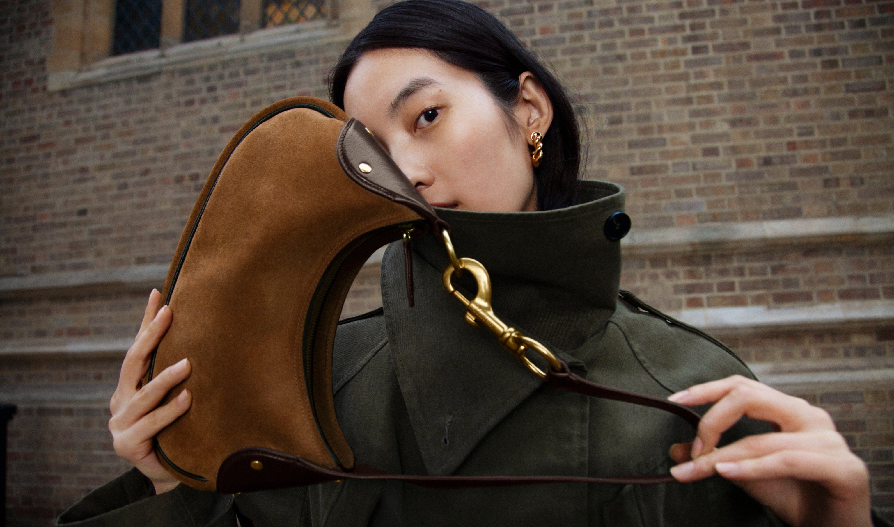 Kleine Hackney-Schultertasche aus Wildleder, die das Gesicht des Models teilweise bedeckt