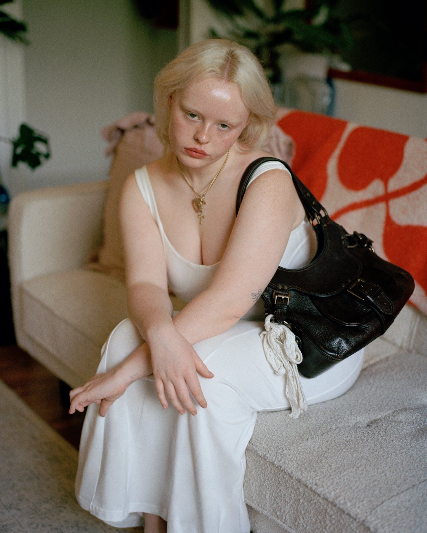 Woman in white dress sitting on a sofa and holding a black Mulberry handbag