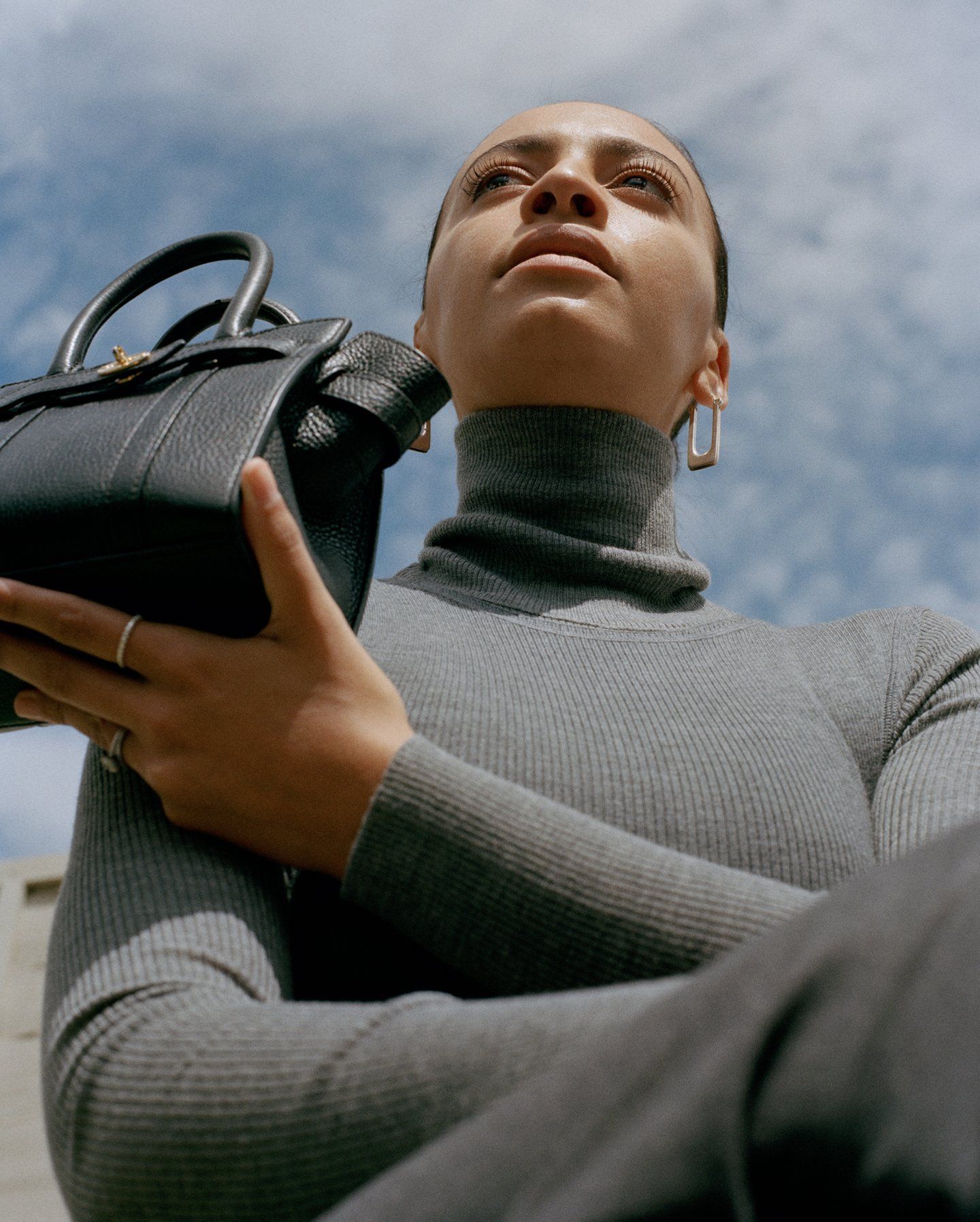 Woman in a grey jumper holding a black Mulberry handbag