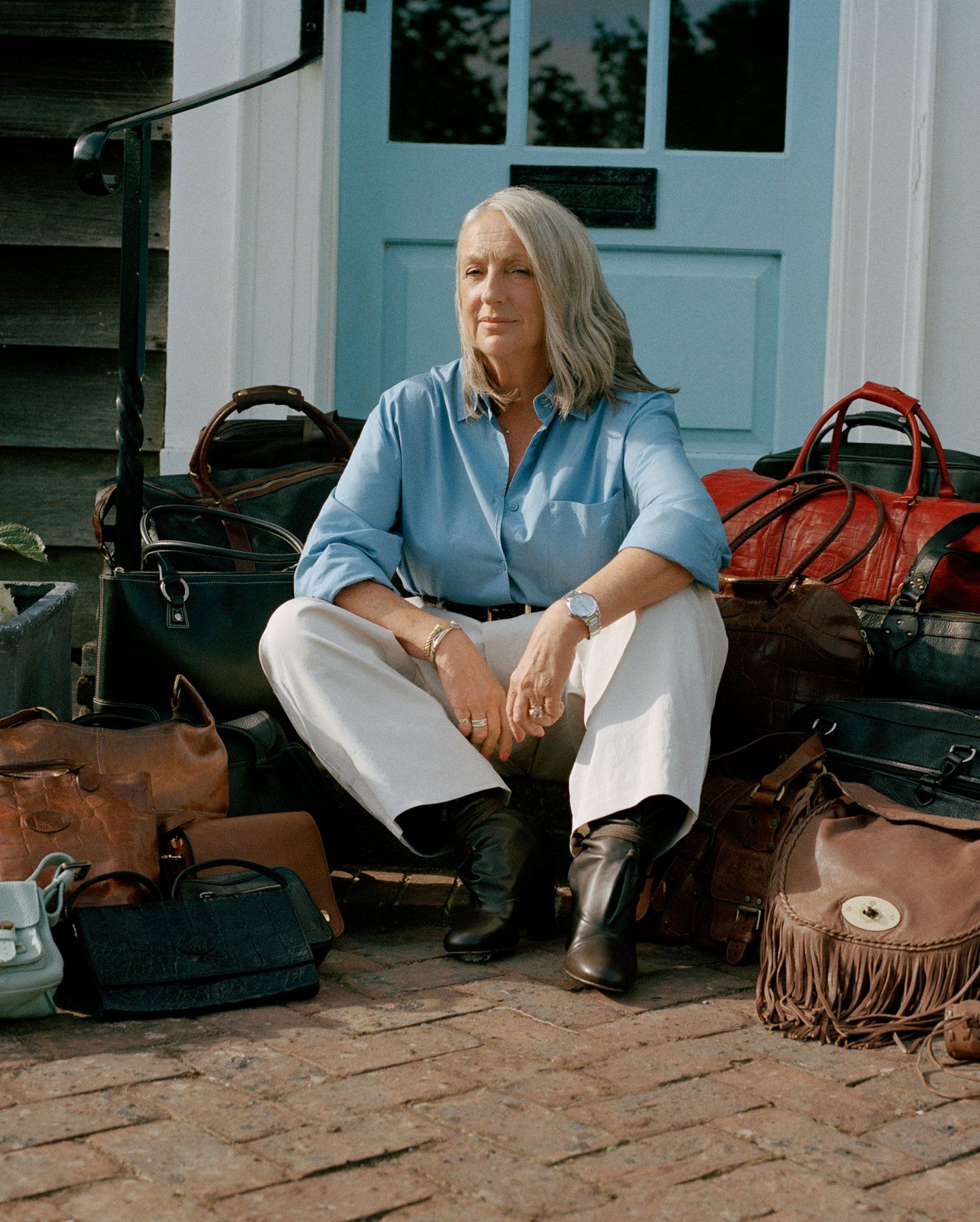 Woman sitting outside her front door surrounded by multiple Mulberry bags