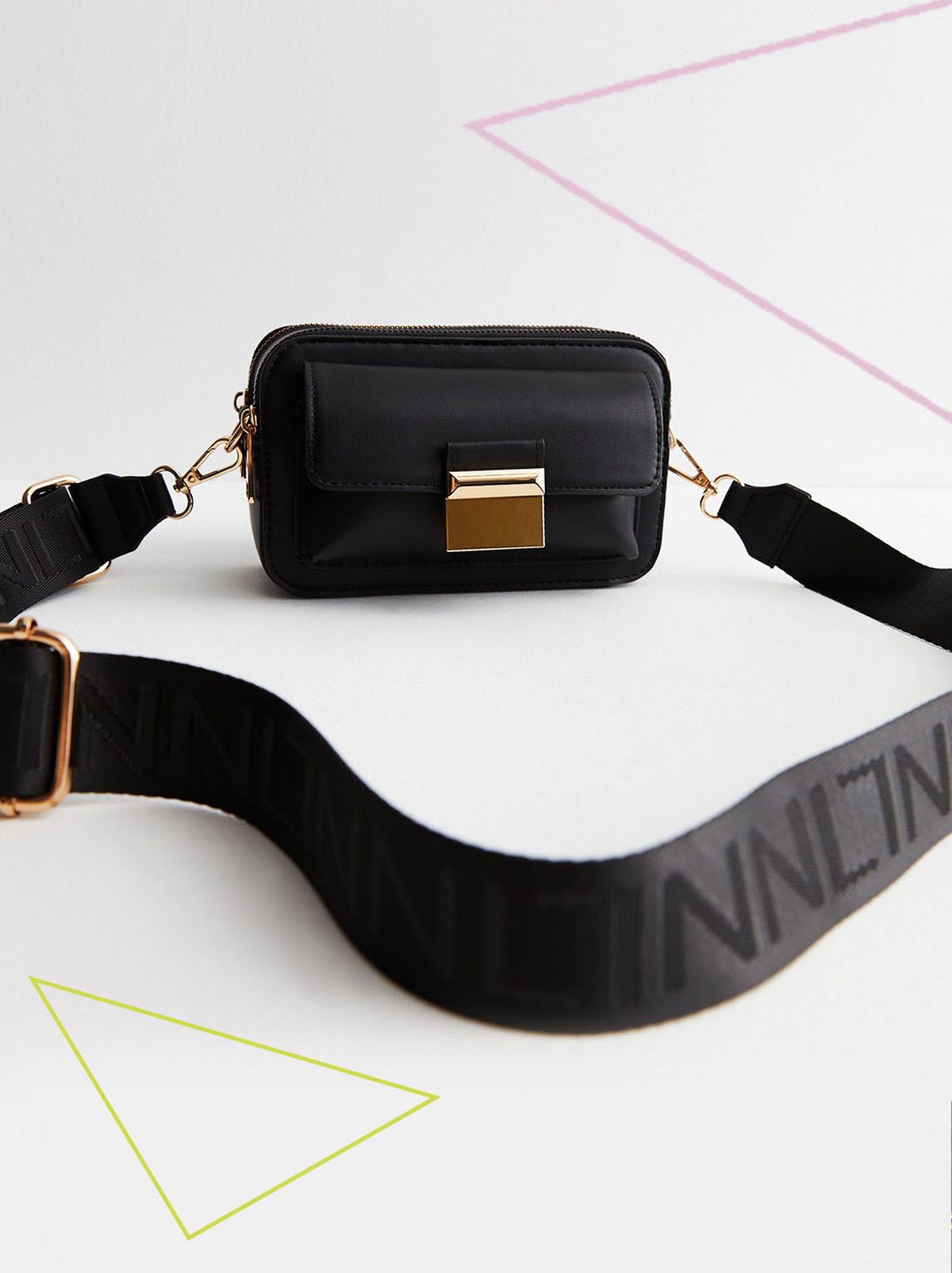 A black logo strap cross body bag is placed on a white floor in front of a white background