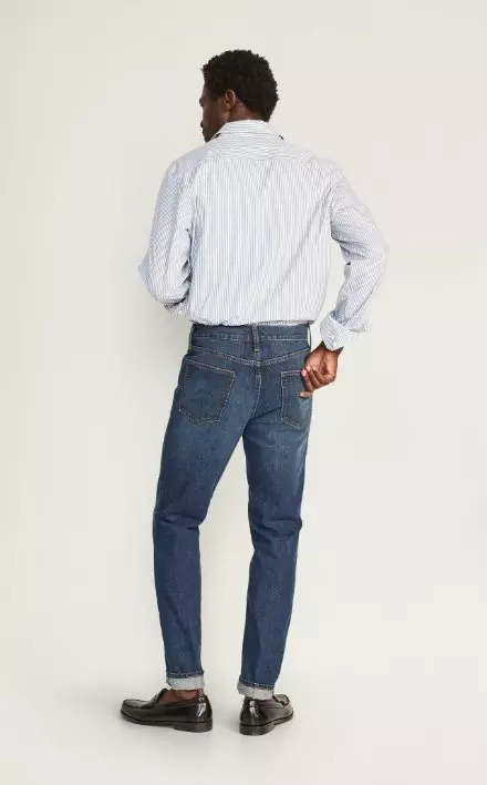A male model wears Athletic Taper style jeans & a light colored long sleeve button-up shirt