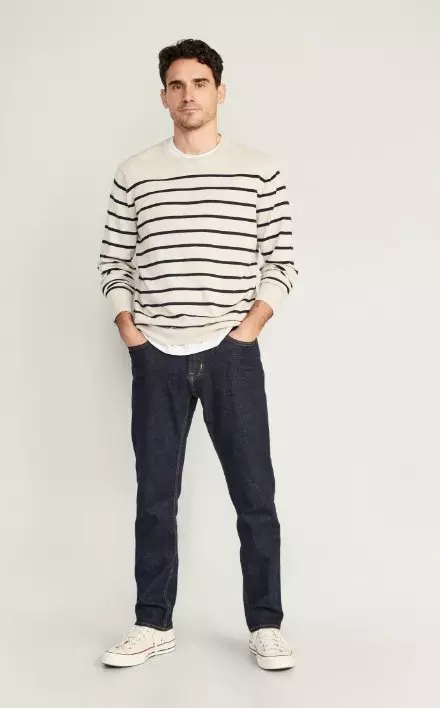 A male model wears dark washed Slim style jeans & a cream colored horizontal striped sweater.