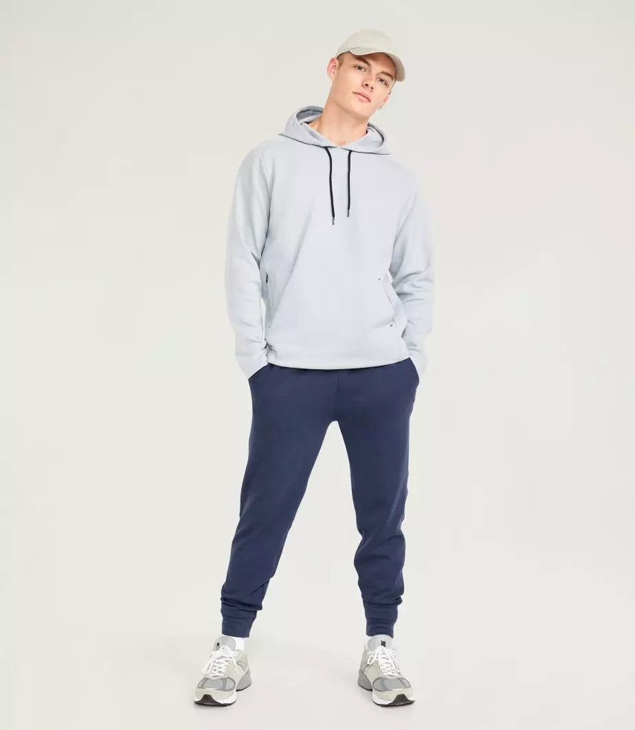 A male model wears dark activewear jogger bottoms and a grey hoodie.