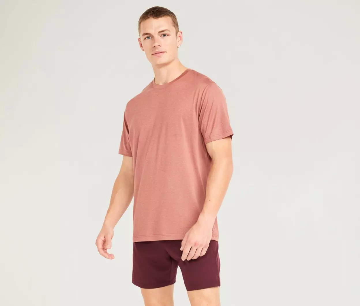 A male model wears a mauve active shirt and maroon shorts.