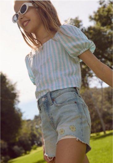 Une jeune fille porte un chemisier à rayures et un short en denim.