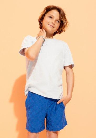 Un jeune garçon porte un t-shirt blanc et un short bleu.
