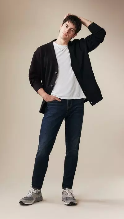 A male model wearing athletic taper jeans and a white t-shirt and navy cardigan.