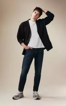 A male model wearing athletic taper jeans and a white t-shirt and navy cardigan.