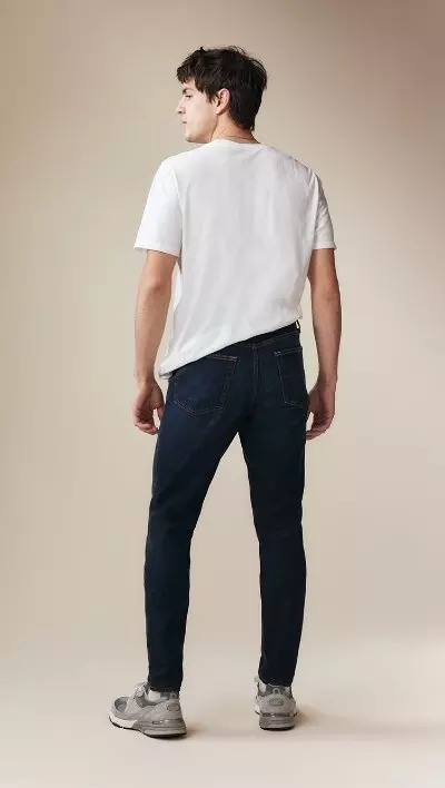 A male model wearing athletic taper jeans and a white t-shirt and navy cardigan.