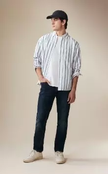 A male model wearing slim jeans and a striped button-down shirt.