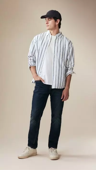 A male model wearing slim jeans and a striped button-down shirt.