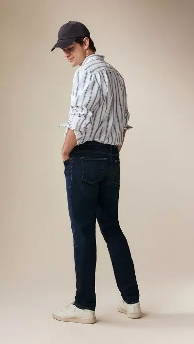 A male model wearing slim jeans and a striped button-down shirt.