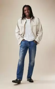 A male model wearing straight jeans and a beige jacket.