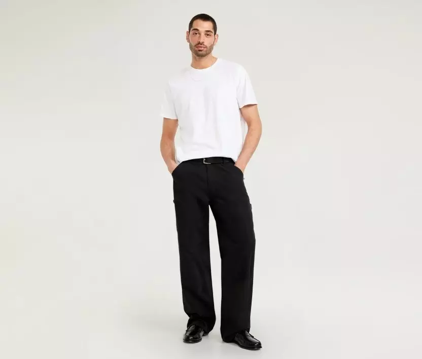 A male model wearing a pair of dark baggy carpenter pants.