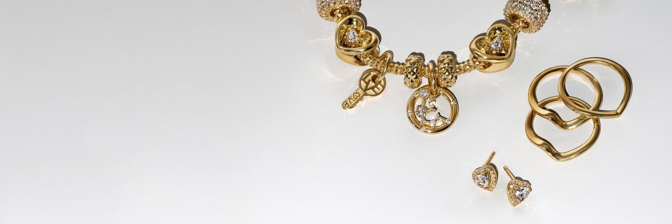 Bild von einem goldenen und mit im Labor gezüchteten Diamanten versehenen Pandora BE LOVE Charm-Armband und fünf Ohrringen