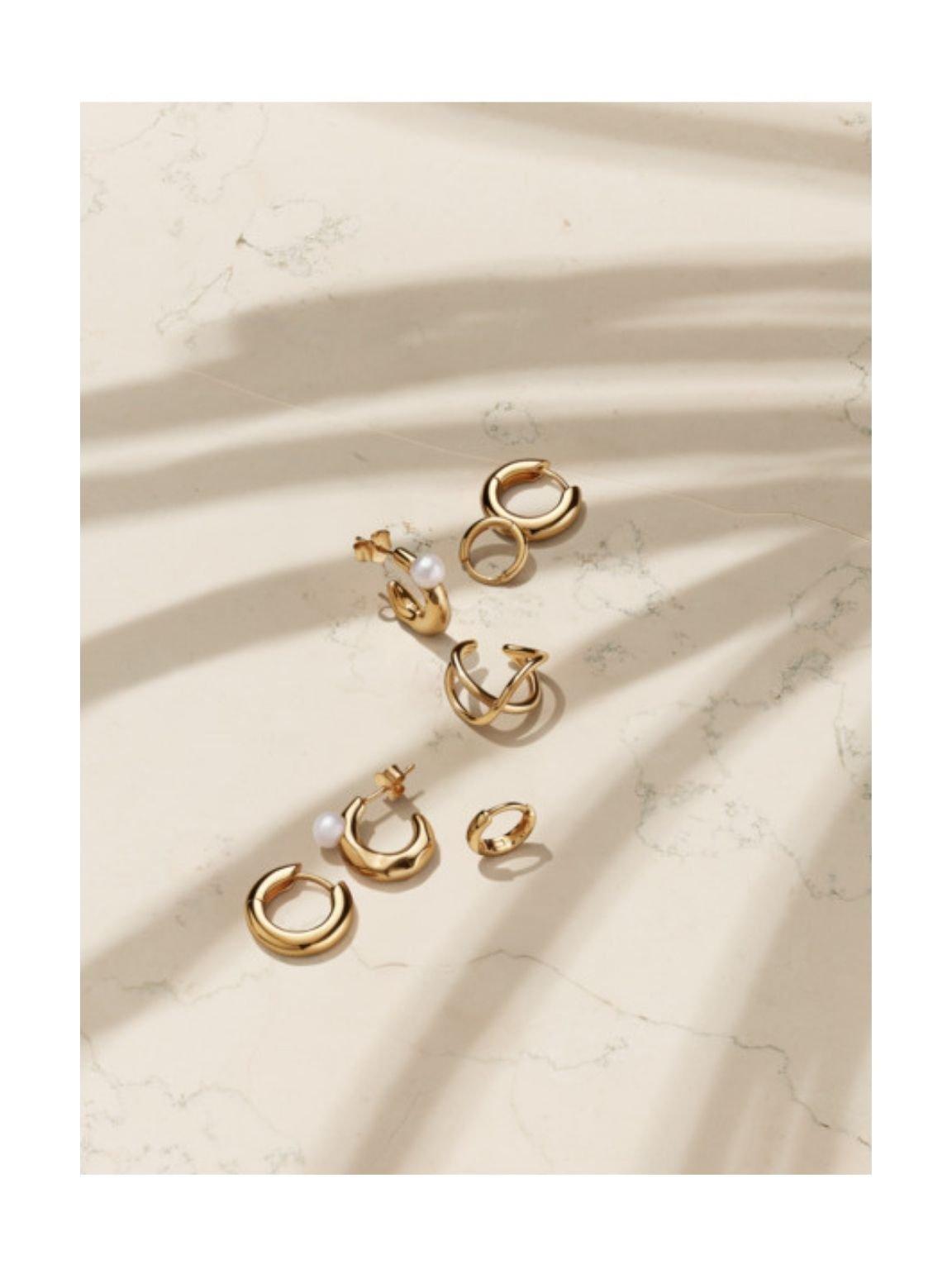 Pandora Essence gold earrings on a beige marble surface