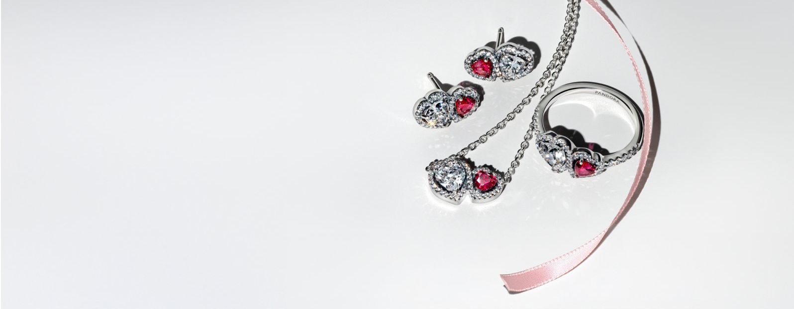 La modelo está de pie con la mano derecha apoyada sobre su cabeza. Lleva una pulsera de charms con un medallón dorado y varios collares de cadena.