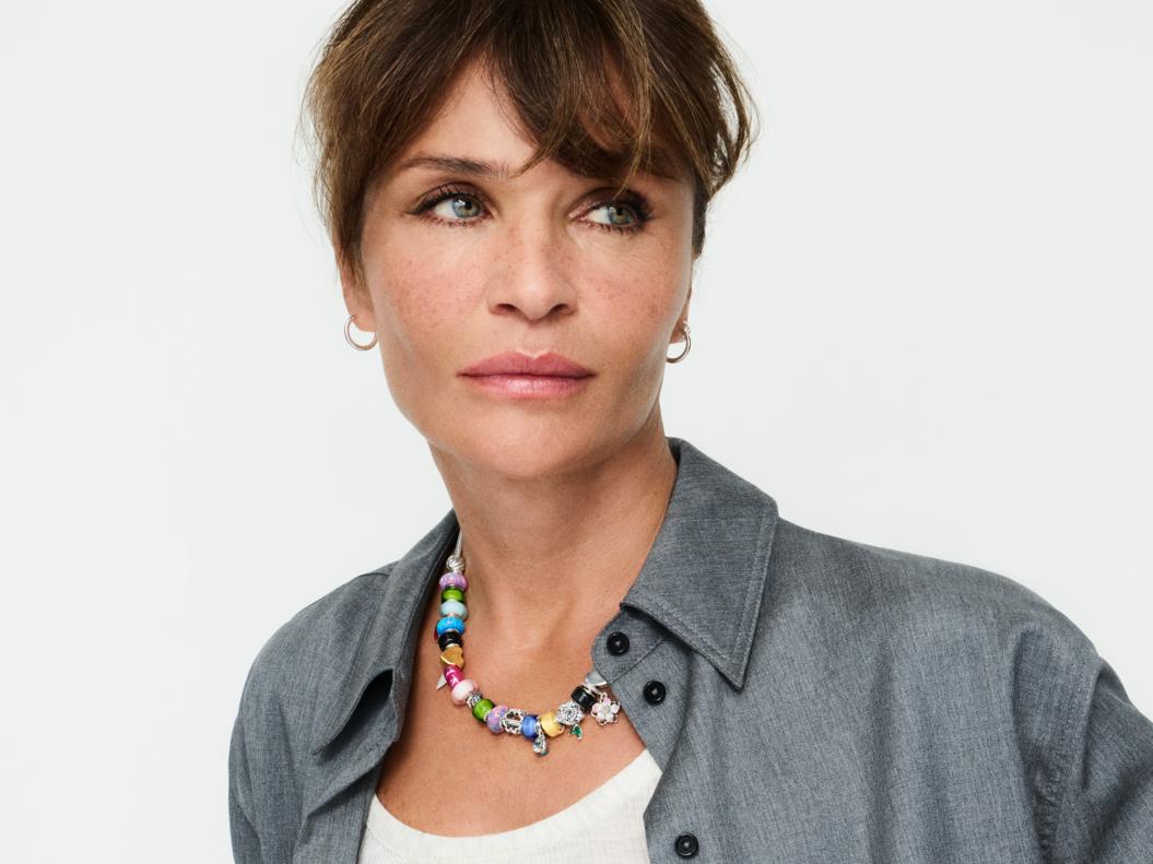 Supermodel Helena Christensen wears a multi-coloured charm necklace with small hoop earrings.