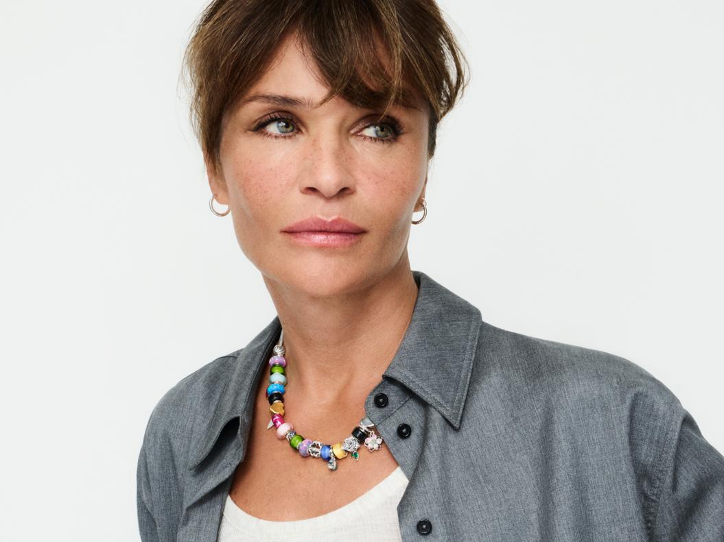 Supermodel Helena Christensen wears a multi-coloured charm necklace with small hoop earrings.