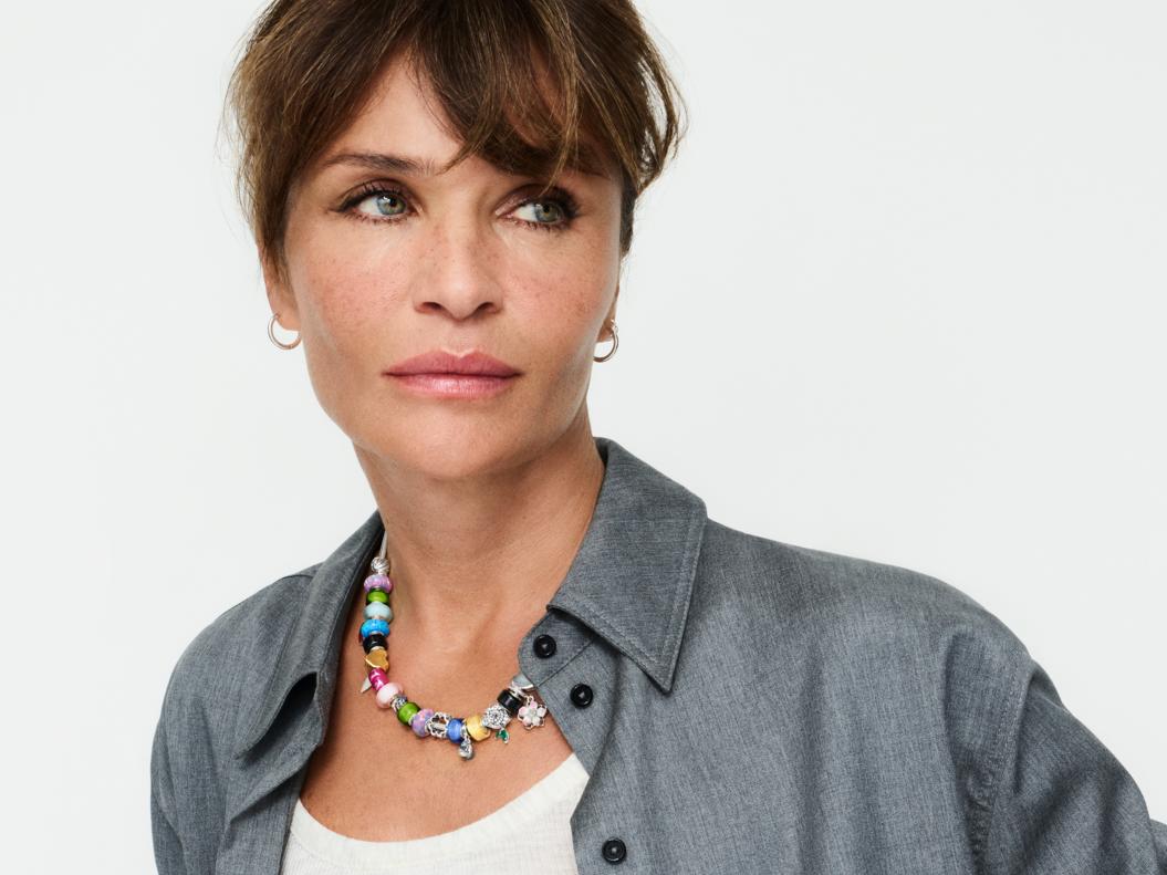 Supermodel Helena Christensen wears a multi-coloured charm necklace with small hoop earrings.