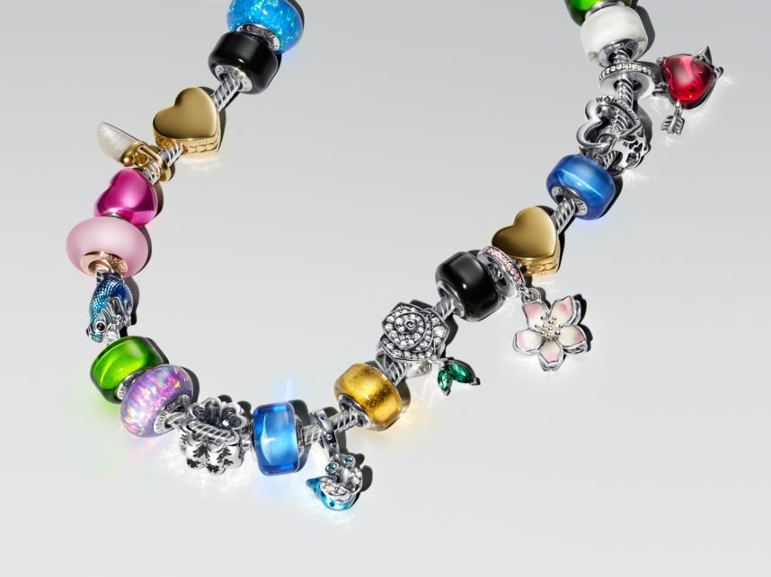 Un bracciale pieno di charm colorati posato su un piano bianco. Il bracciale multicolore presenta charm blu, rosa e in oro.