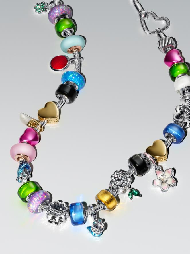 Un bracciale pieno di charm colorati posato su un piano bianco. Il bracciale multicolore presenta charm blu, rosa e in oro.