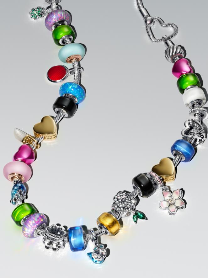 A colourful charm bracelet lays on a flat, white surface. The multi-coloured bracelet features blue, pink and gold charms.