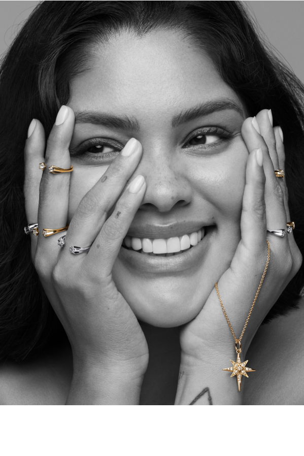 Model smiling with hands on her face, showcasing a sterling silver rings stack and a pendant necklace in her left hand.