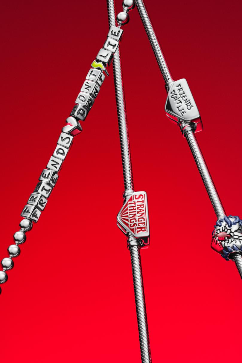 Three sterling silver chains decorated with Stranger Things charms against a red background.