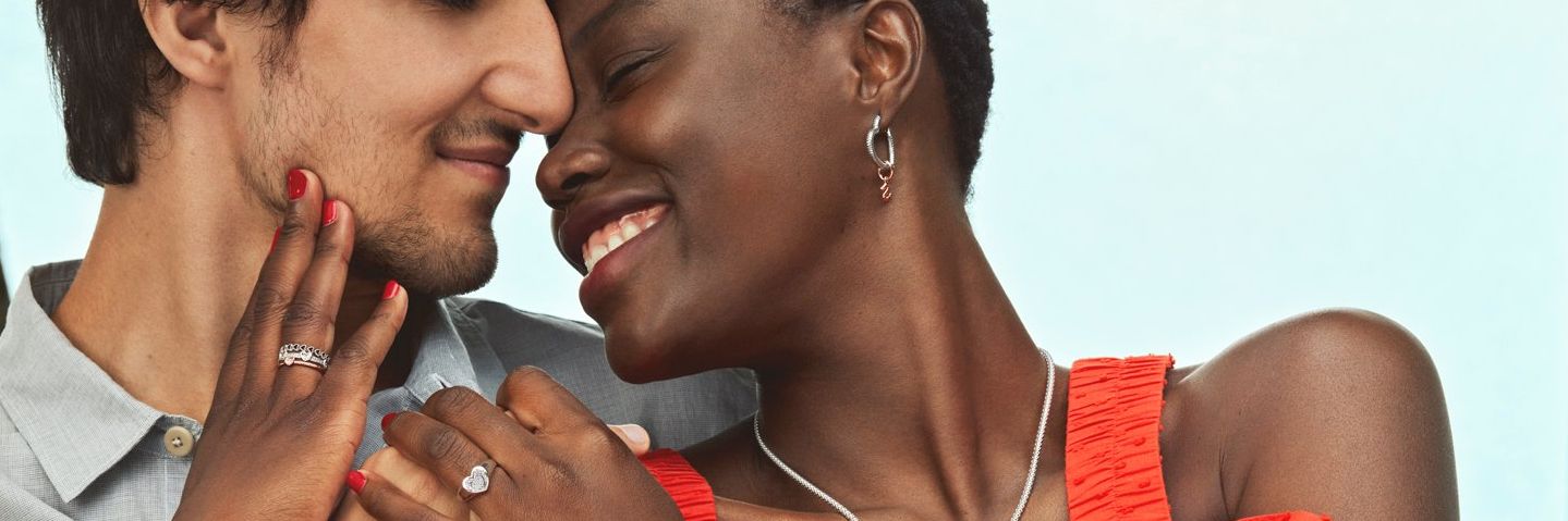 smiling women wearing bracelet, necklace, and earrings hugs a man