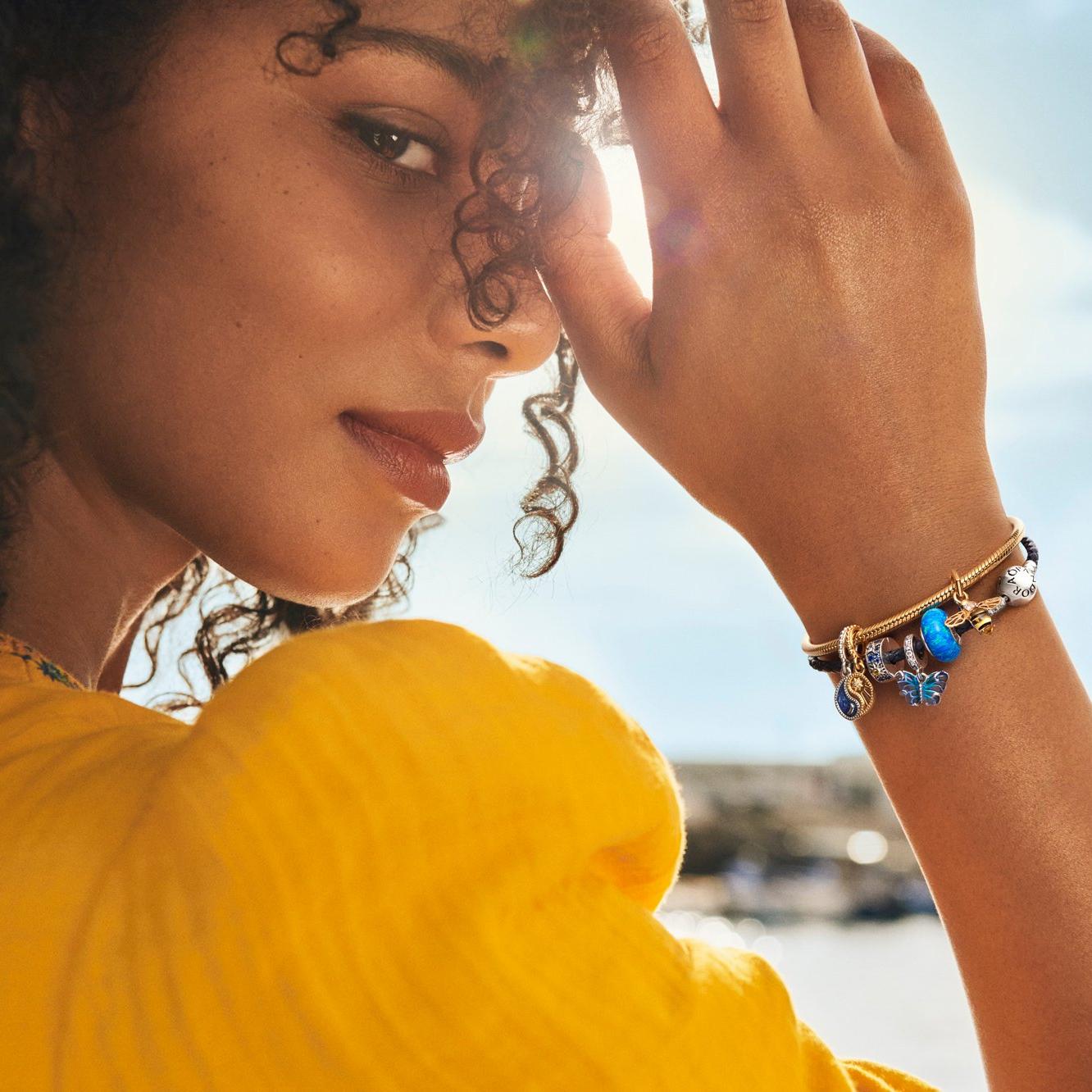 Smiling woman with colourful blue charms on bracelet.