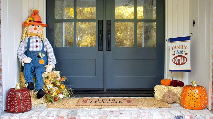 Front door decorated with a scarecrow, hay bales, football flag, a fall welcome mat, and pumpkins