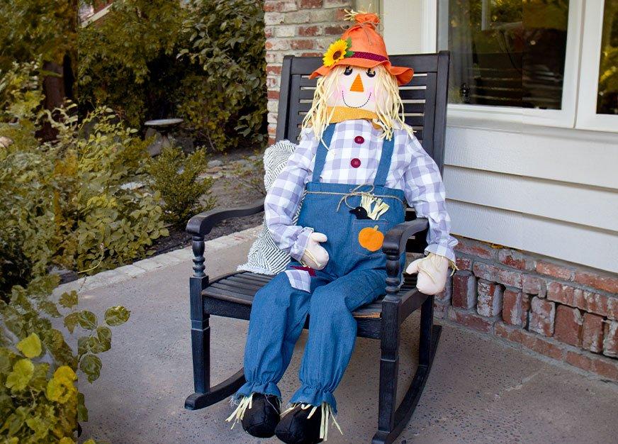 Scarecrow sitting in a rocking chair on a porch