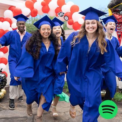 Group of graduates wearing blue cap and gowns smiling and dancing.