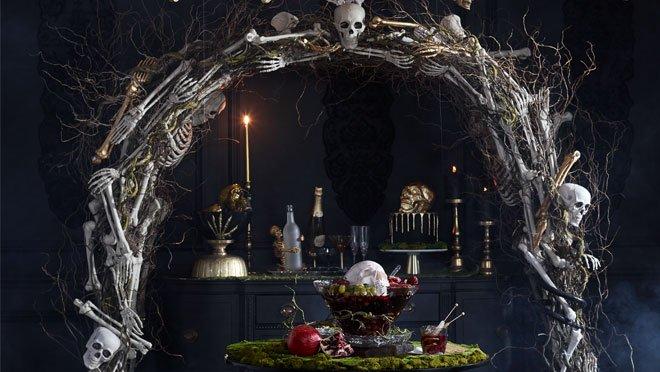 Party Decorated in Boneyard Glam Style with Large Arch Made of Skeleton Bones and Skeleton Themed Party Supplies Like Candles.