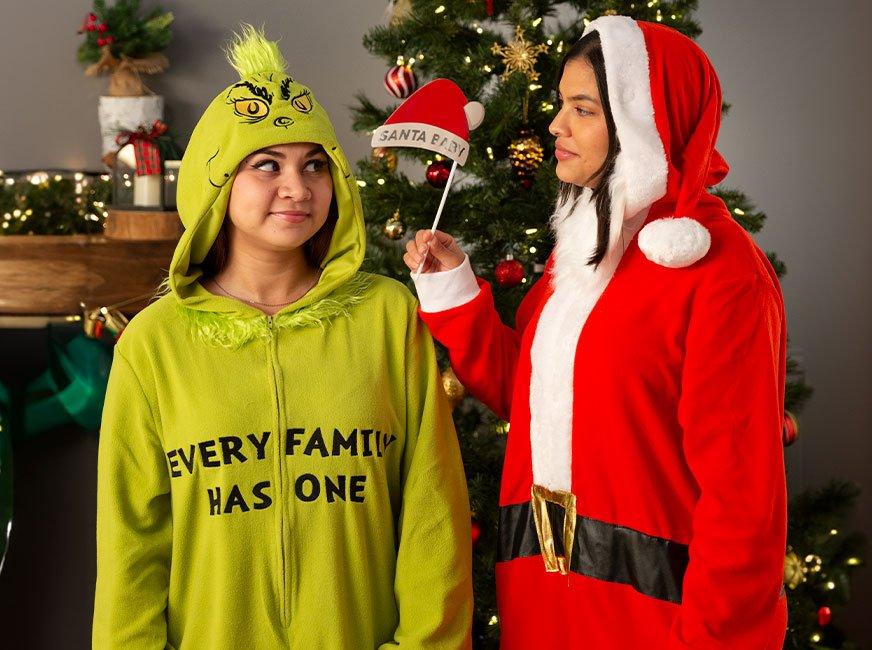 A young women dressed in a Grinch onesie and another young women dress in a santa onesie