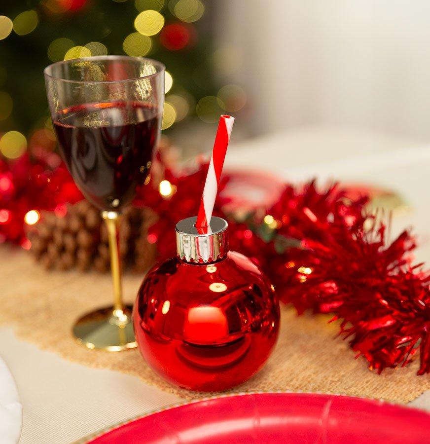 Festive glassware, a gold stemmed wine glass and a red ornament with a drinking straw