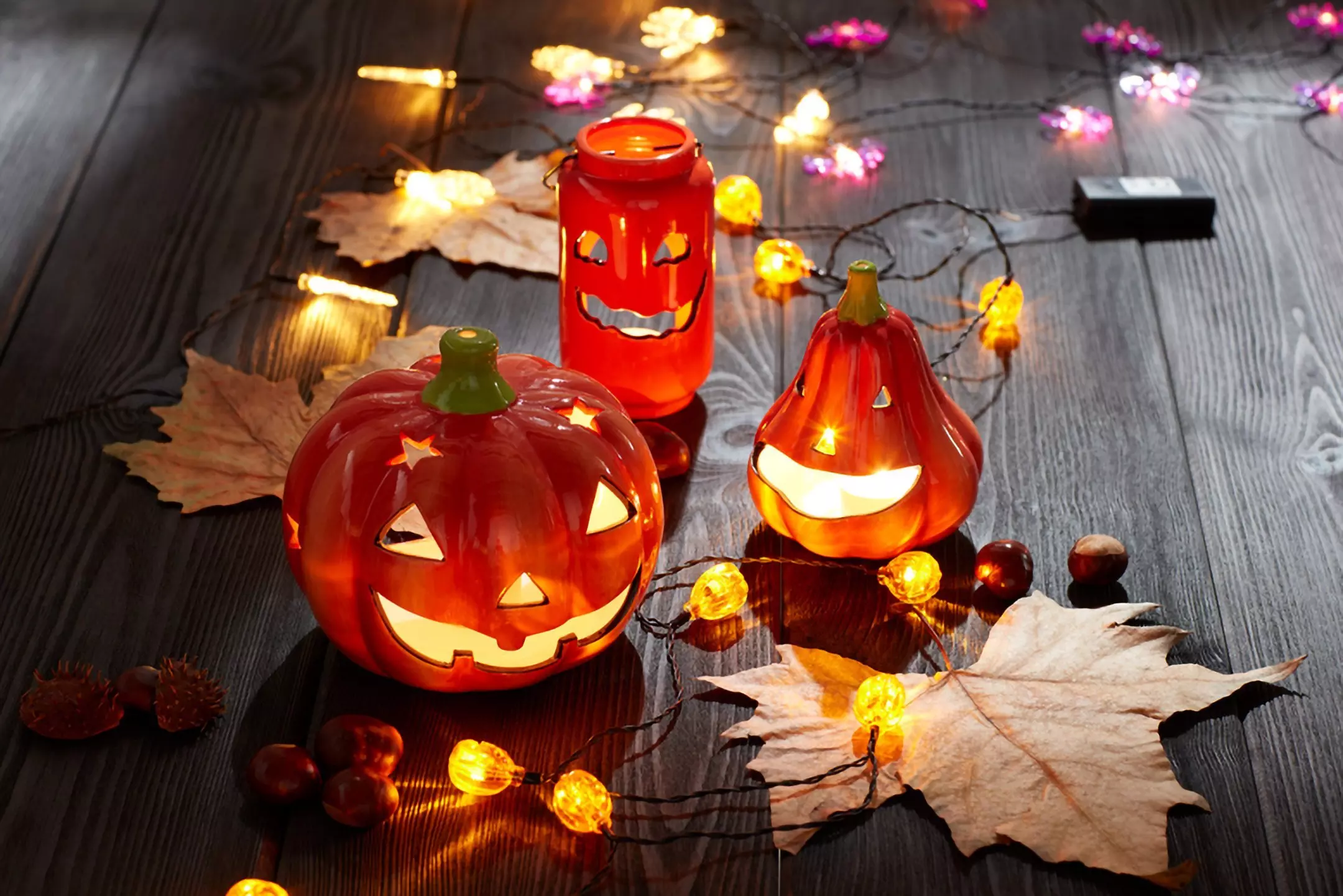 Pepco Halloween decorative lanterns shaped as pumpkins and jar with glowing faces, surrounded by autumn leaves and string lights.