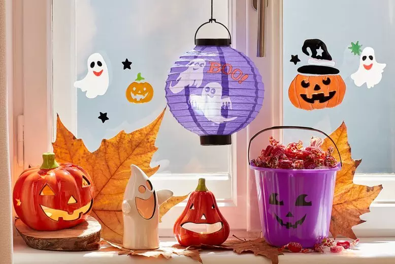 Halloweenowe dekoracje Pepco na parapecie: lampion-dynia, świecznik-duch, papierowy lampion, fioletowe wiadro i naklejki na okno.