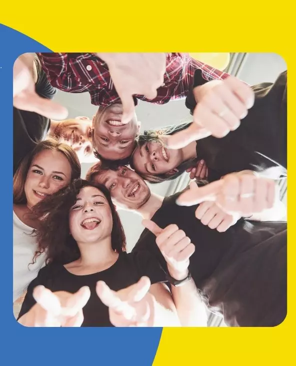 Grup de tineri zâmbitori cu degetele mari ridicate, văzuți de jos în cerc.