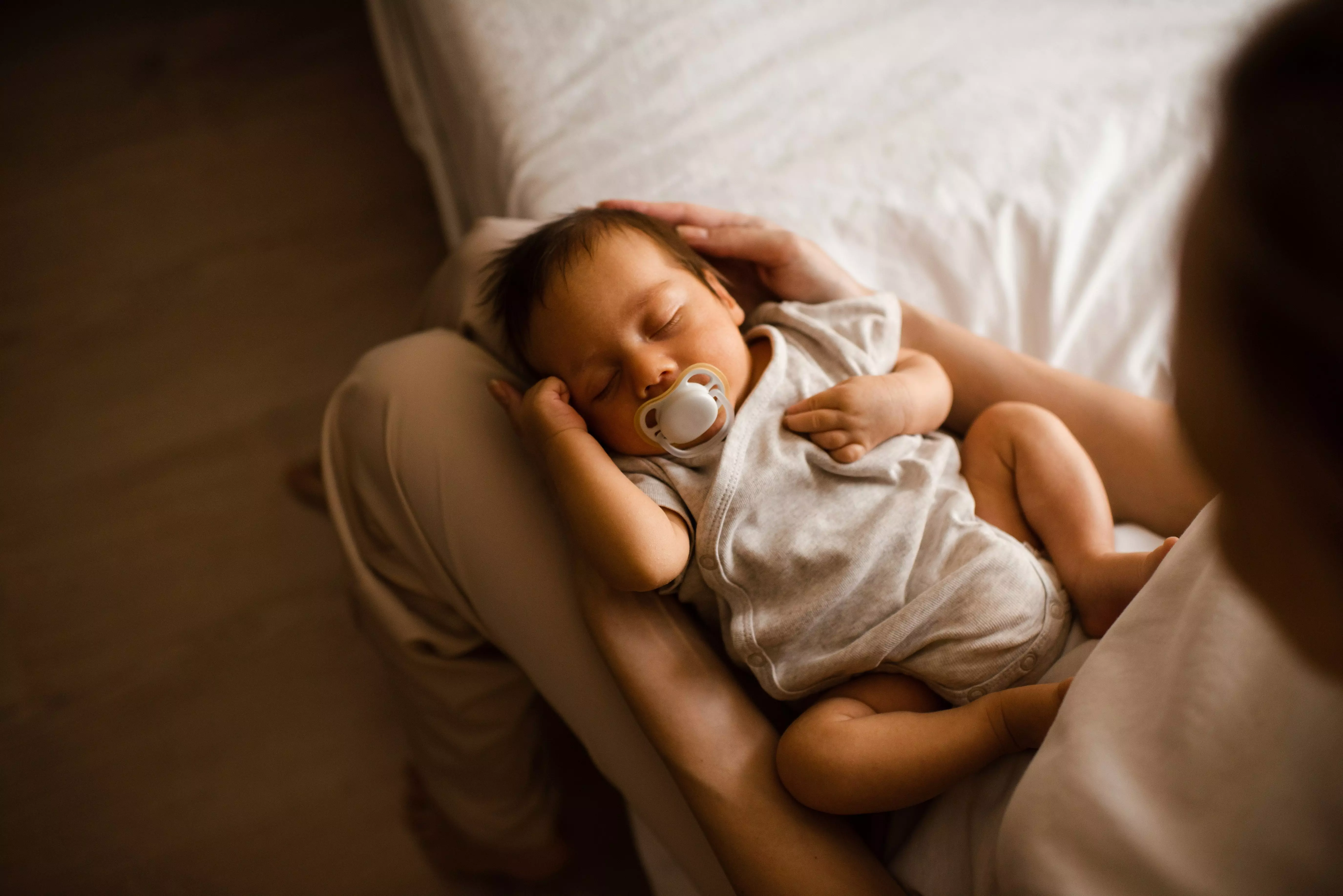 Pepco baby sleeping peacefully with dummy whilst being cradled in parent's arms.